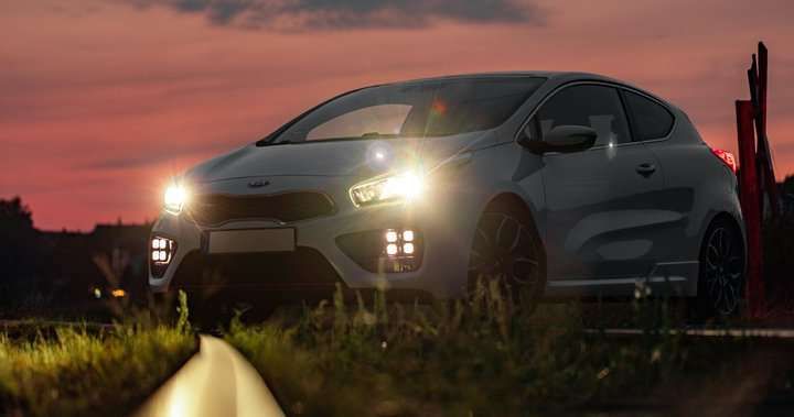 A white car parked with bright LED headlights glowing at sunset.