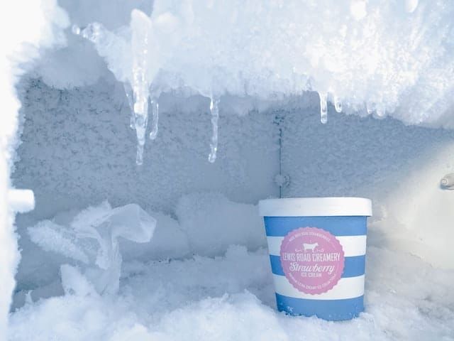 A container of strawberry ice cream surrounded by frost and ice icicles.