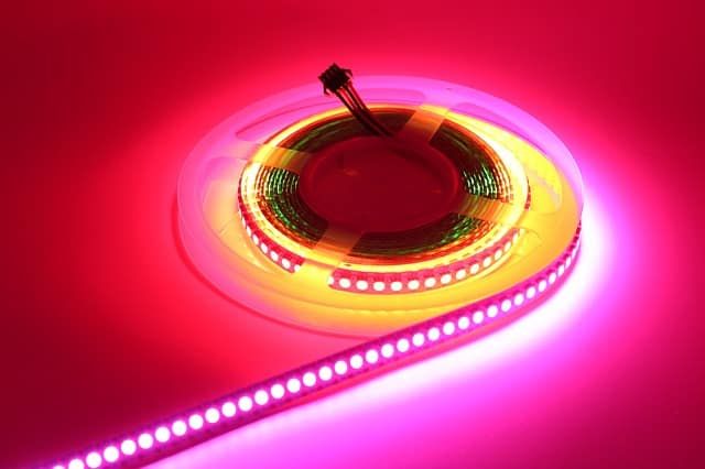 A coil of colorful LED strip lights on a pink background.