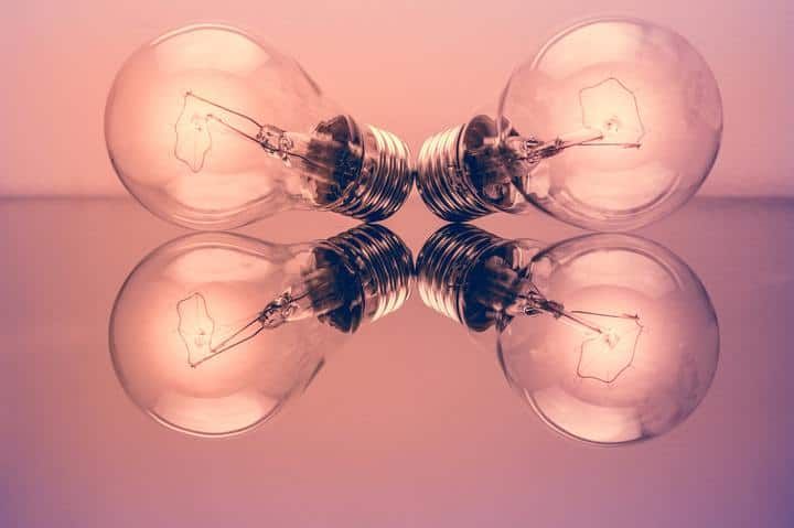 Two vintage light bulbs facing each other on a reflective surface.