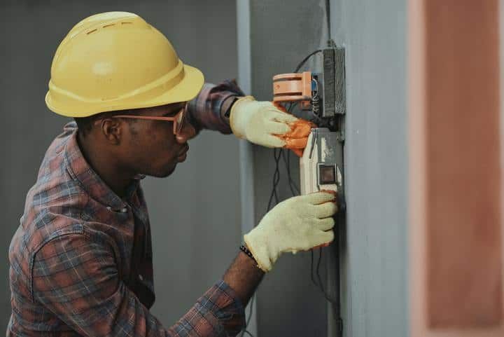 A worker in a yellow hard hat repairs LED lighting wiring on a wall.