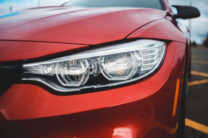 Close-up of a sleek red car's LED headlights and front design.