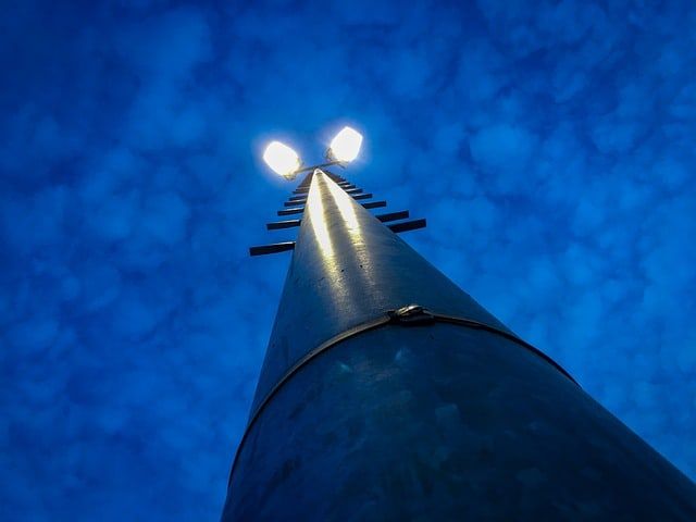 A tall light pole illuminated against a blue sky with clouds.