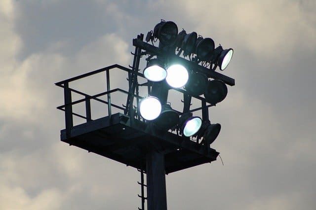 Bright LED floodlights mounted on a tall platform against a cloudy sky.