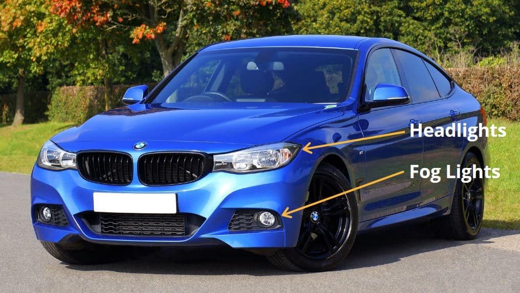 A blue BMW car showing headlights and fog lights on a sunny day.