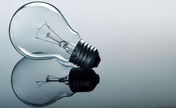 A glass light bulb lying on a reflective surface, showcasing its elegant shape.