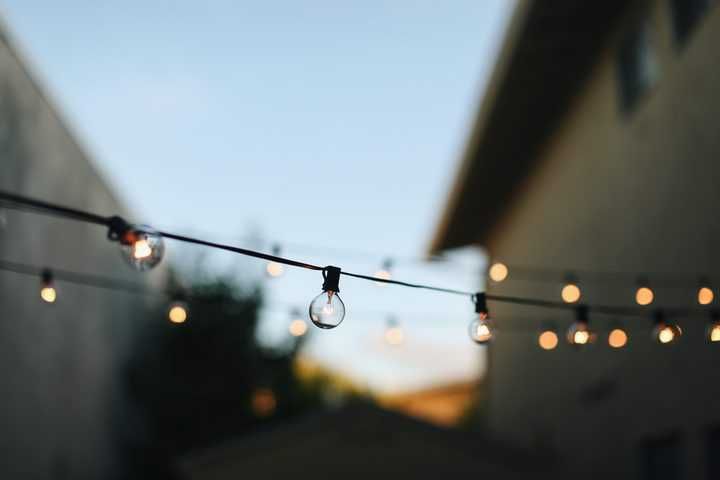 String lights hang between buildings, illuminating a soft evening sky.