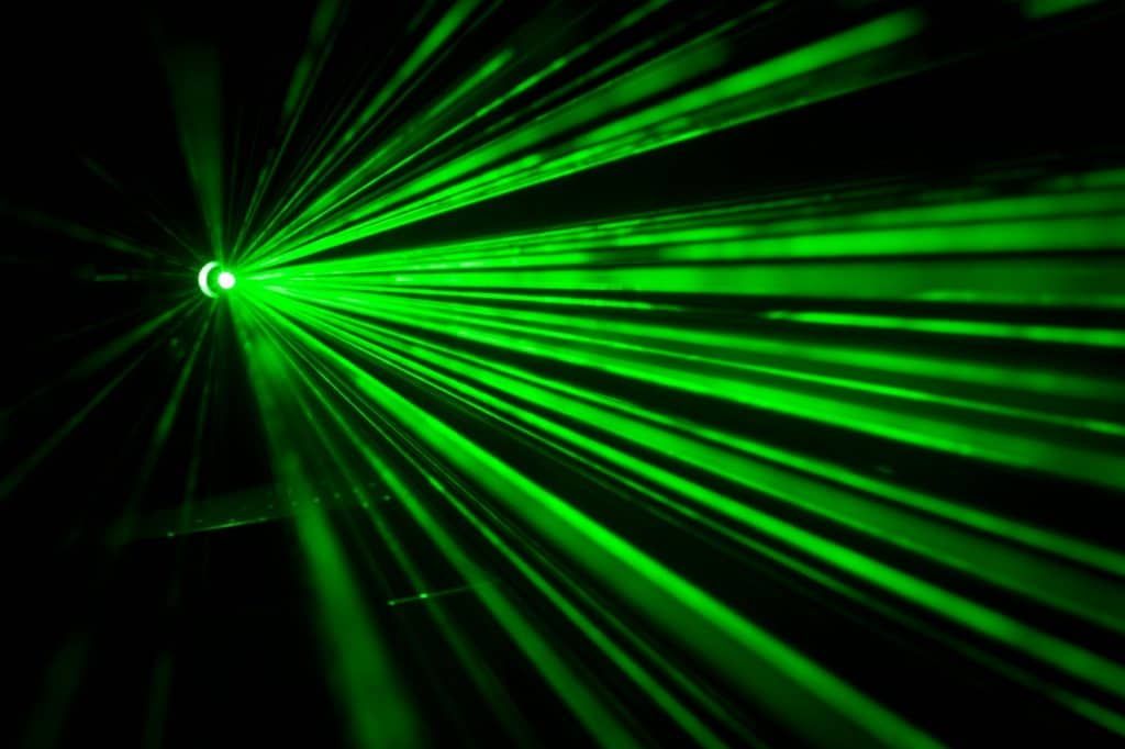 Bright green laser beams emanate from a central point in darkness.