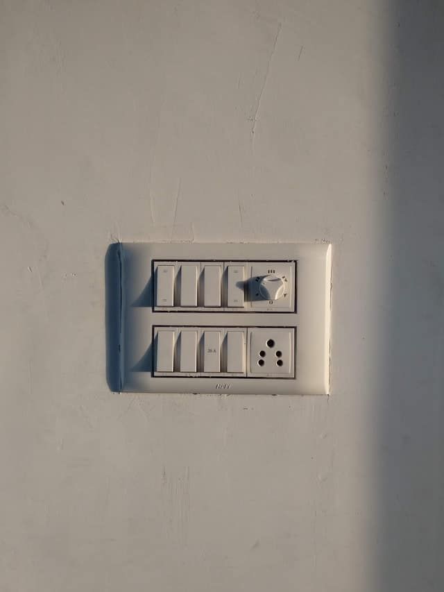 A white wall with a panel of light switches and an electrical outlet.