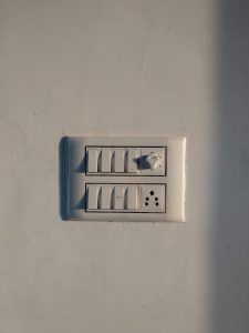 White wall switch panel with multiple dimmer switches and an electrical outlet.