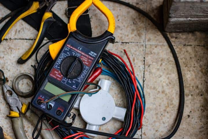 Clamp meter surrounded by various electrical wires and tools on a surface.