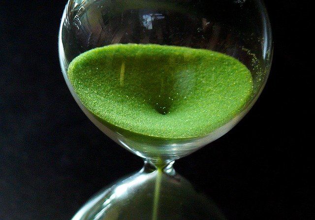 An hourglass filled with green sand, showing time passing.