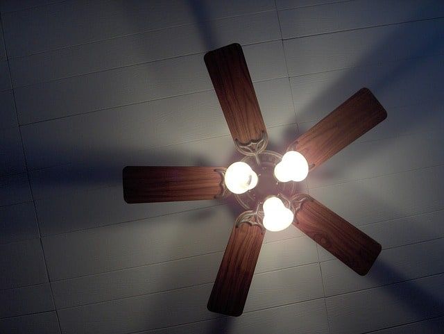A ceiling fan with four wooden blades and three bright bulbs.