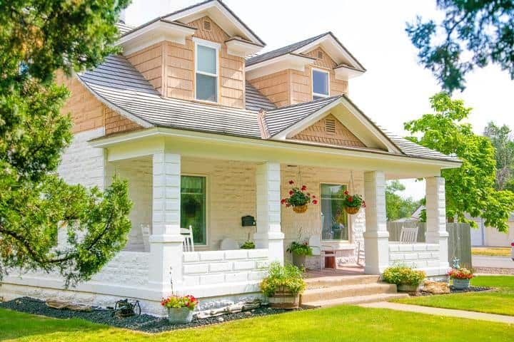 Bright, welcoming house with a porch, flower pots, and lush green grass.