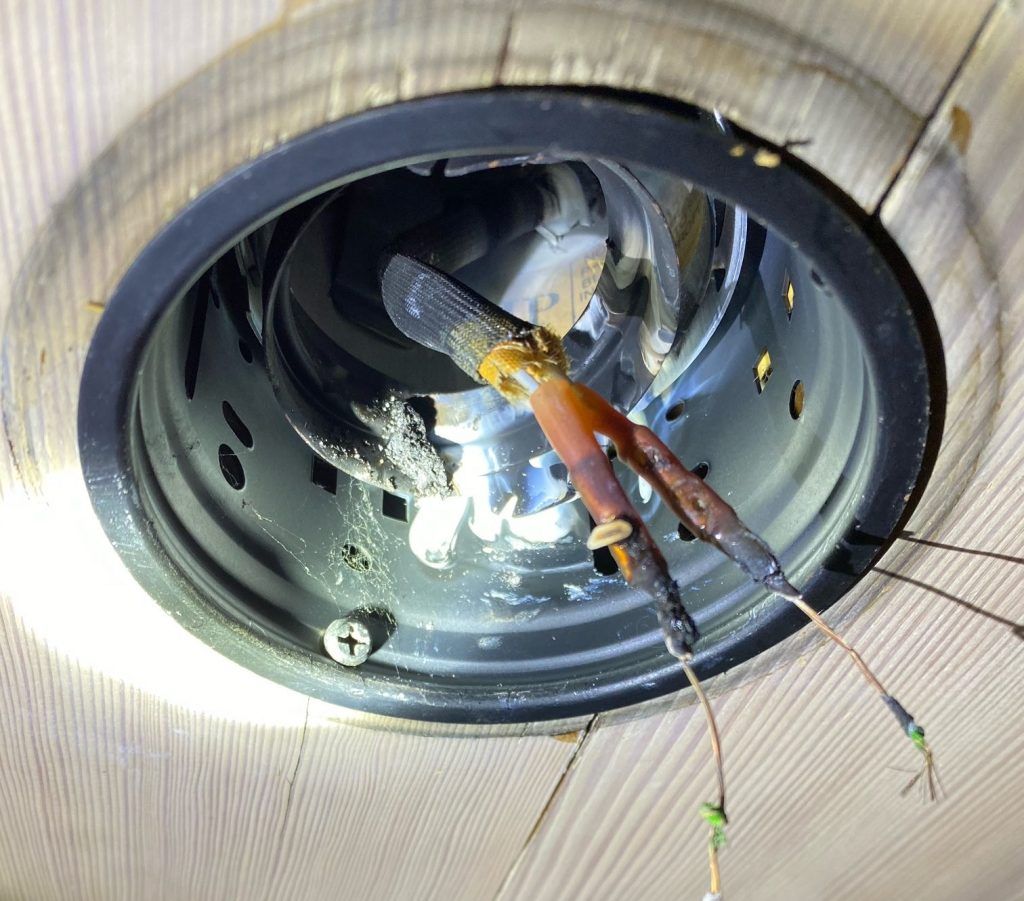 Close-up of exposed wires and light fixture inside a ceiling space.