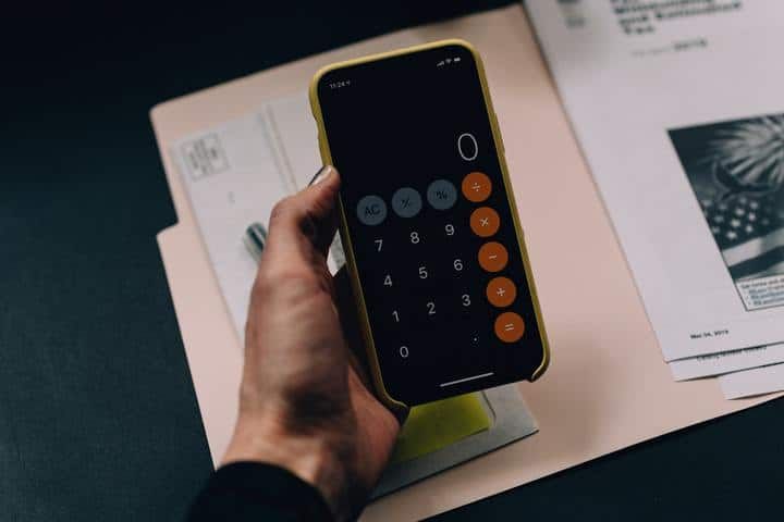 A hand holding a smartphone calculator displaying the number zero.