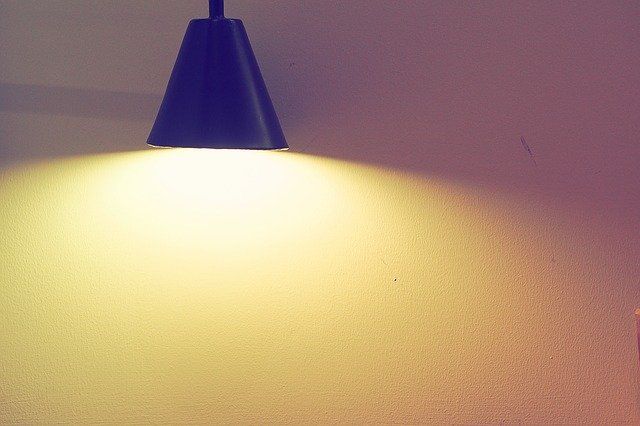 A black pendant light illuminating a textured wall with warm light.