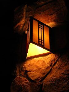 A modern wall-mounted light fixture glowing warmly against stone.
