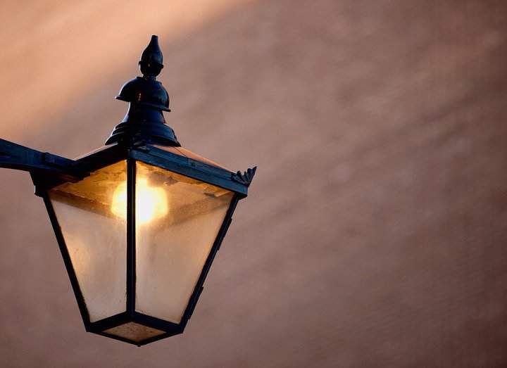 A decorative street lamp with a glowing bulb illuminating a warm background.