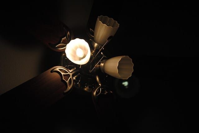Ceiling fan with decorative light fixtures illuminated against a dark background.