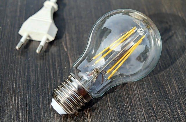 Clear LED bulb with yellow filaments next to an electrical plug.