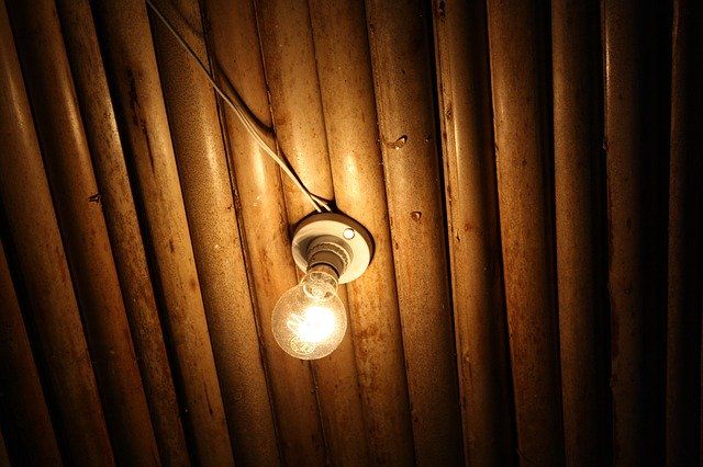 A glowing light bulb hangs from a ceiling with wooden slats.