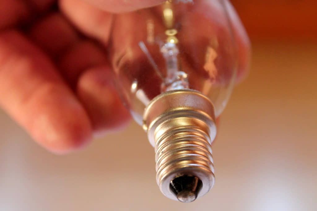A hand holds an LED light bulb with metal base and clear glass.