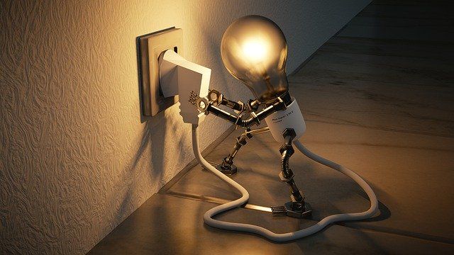 A quirky lamp figure connecting to an electrical outlet with a glowing bulb.