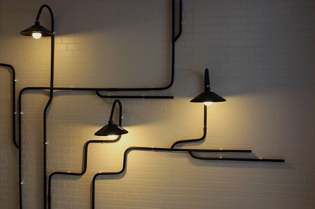 Three stylish black wall lamps connected by curved black pipes on a light wall.