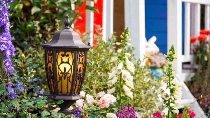 A decorative lantern glows amidst colorful flowers in a garden setting.