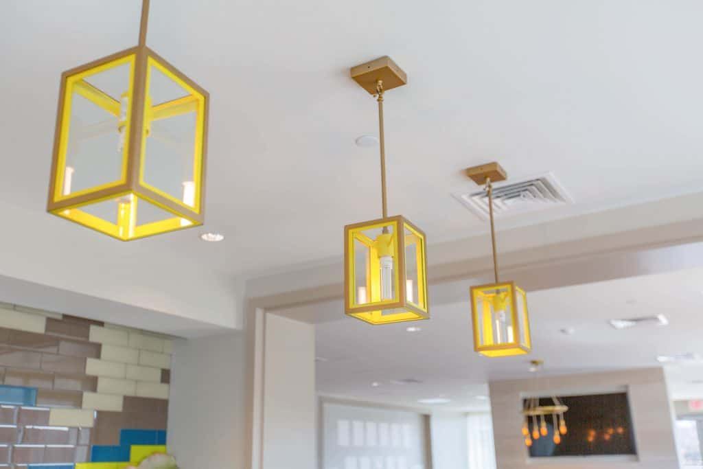 Three hanging yellow lantern-style light fixtures in a modern space.