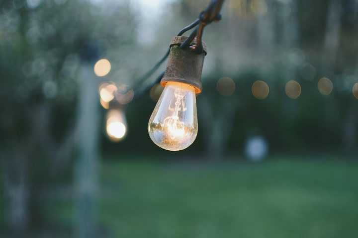 A soft glowing light bulb hangs on a wire against a blurred green background.
