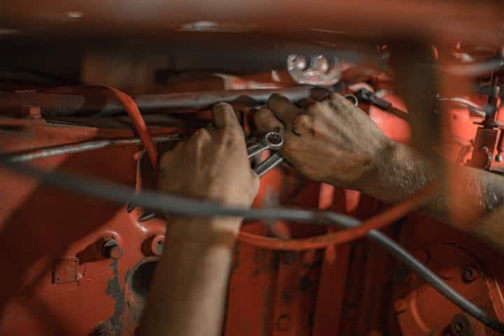 Hands working with tools among red machinery and electrical wires.