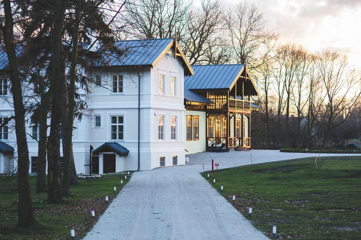 A white house with a blue roof beside a gravel path and trees.