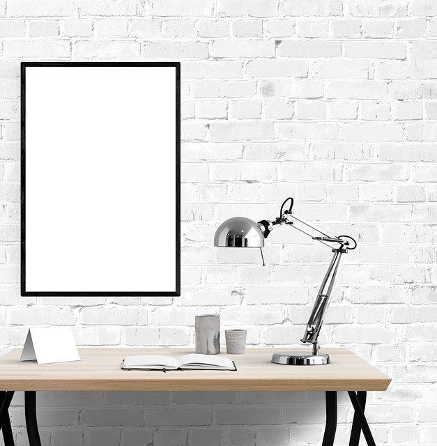 Minimalist desk setup with a lamp, notebook, and empty frame.