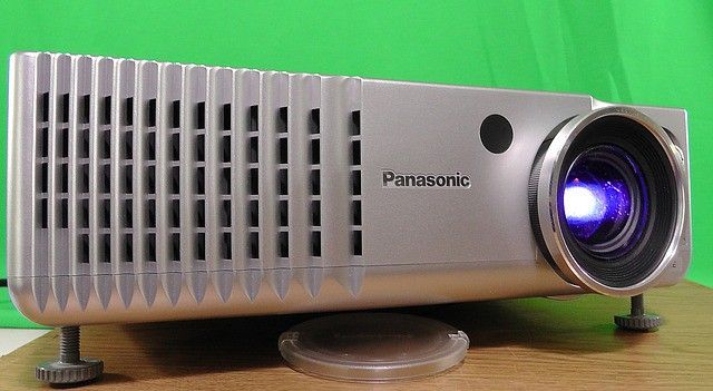 A Panasonic projector with silver casing and visible lens on a wooden surface.