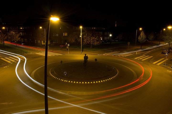 Night view of a roundabout with illuminated paths and light trails from vehicles.