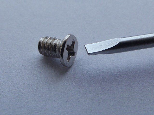 A silver screw next to a flathead screwdriver on a light background.