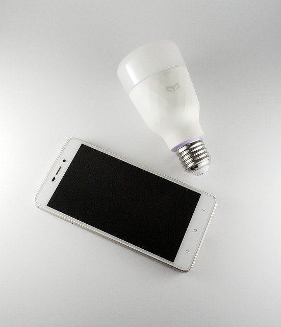 A smart LED bulb beside a smartphone on a light background.