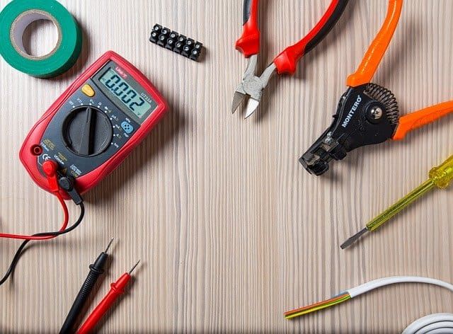 Workspace with a multimeter, tools, and various electrical components on a wooden surface.