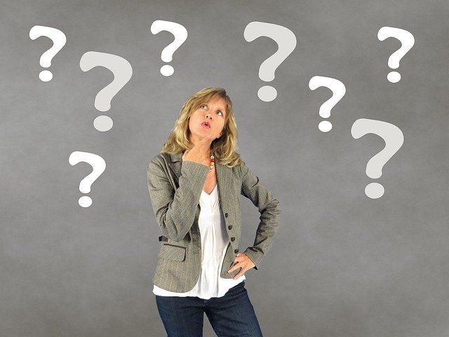 A woman stands thinking with question marks floating around her.