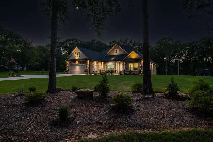 A well-lit house at night surrounded by trees and manicured lawn.